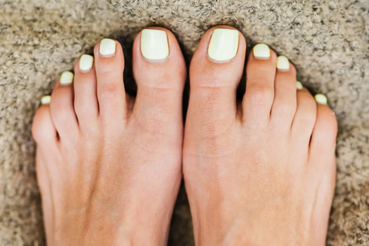 Verzorgde voeten met gelakte nagels op een zacht vloerkleed thuis